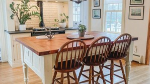 A kitchen with a central island, wooden chairs, white cabinets, and a chandelier. - A rambling farmhouse, now a modern and comfortable sanctuary for you to enjoy! (Harpswell)