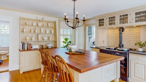 A spacious kitchen with a large island, wooden chairs, white cabinetry, and a chandelier. - A rambling farmhouse, now a modern and comfortable sanctuary for you to enjoy! (Harpswell)