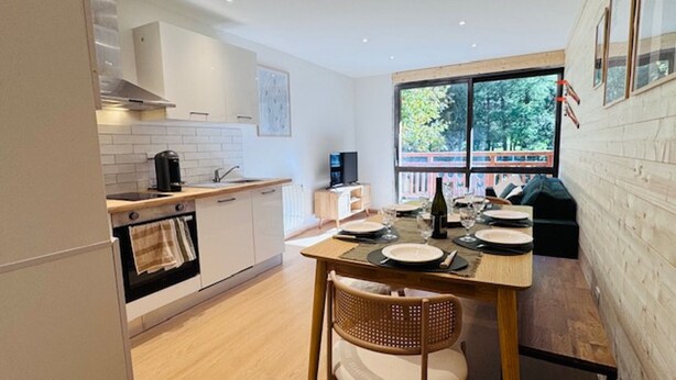 A modern kitchen with white cabinets, a dining table set for four, and a large window offering a view of greenery outside. - Renovated apartment for 6 near slopes - Les 2 Alpes (Les Deux Alpes)