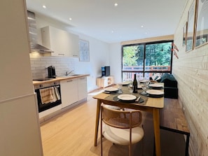 Una cocina moderna con armarios blancos, una mesa de comedor preparada para cuatro personas y un amplio ventanal con vistas al exterior.