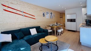 A modern living room with a sofa, a small round table, and a dining area with a table and chairs. - Renovated apartment for 6 near slopes - Les 2 Alpes (Les Deux Alpes)