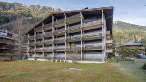 Un hotel de varios pisos con balcones, ubicado en una zona montañosa con un patio cubierto de césped.