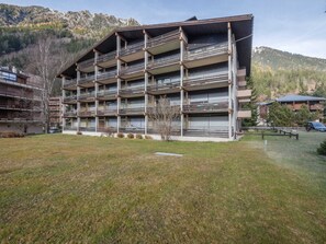 A multi-story hotel with balconies, situated in a mountainous area with a grassy courtyard. - Spacious apartment with parking and pets allowed, near Chamonix (Chamonix-Mont-Blanc)