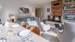 Una sala de estar moderna con chimenea, un comedor con mesa dispuesta para cuatro personas y una zona de estar acogedora con sofá y sillones.