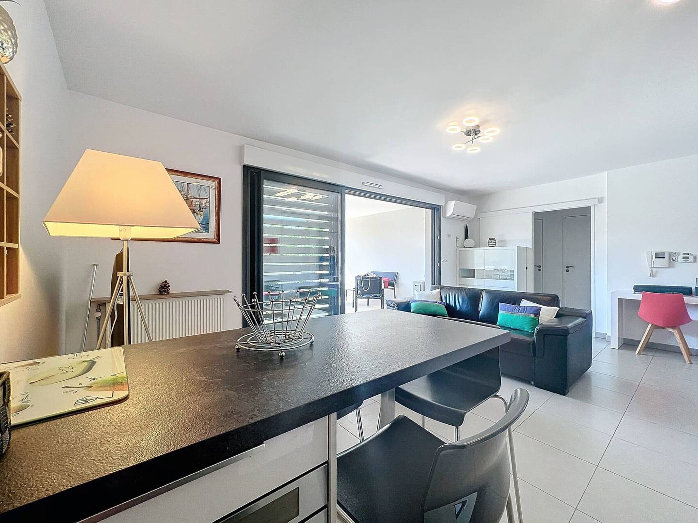 A modern kitchen with a central island, a dining area with chairs, a sofa, and a red chair.