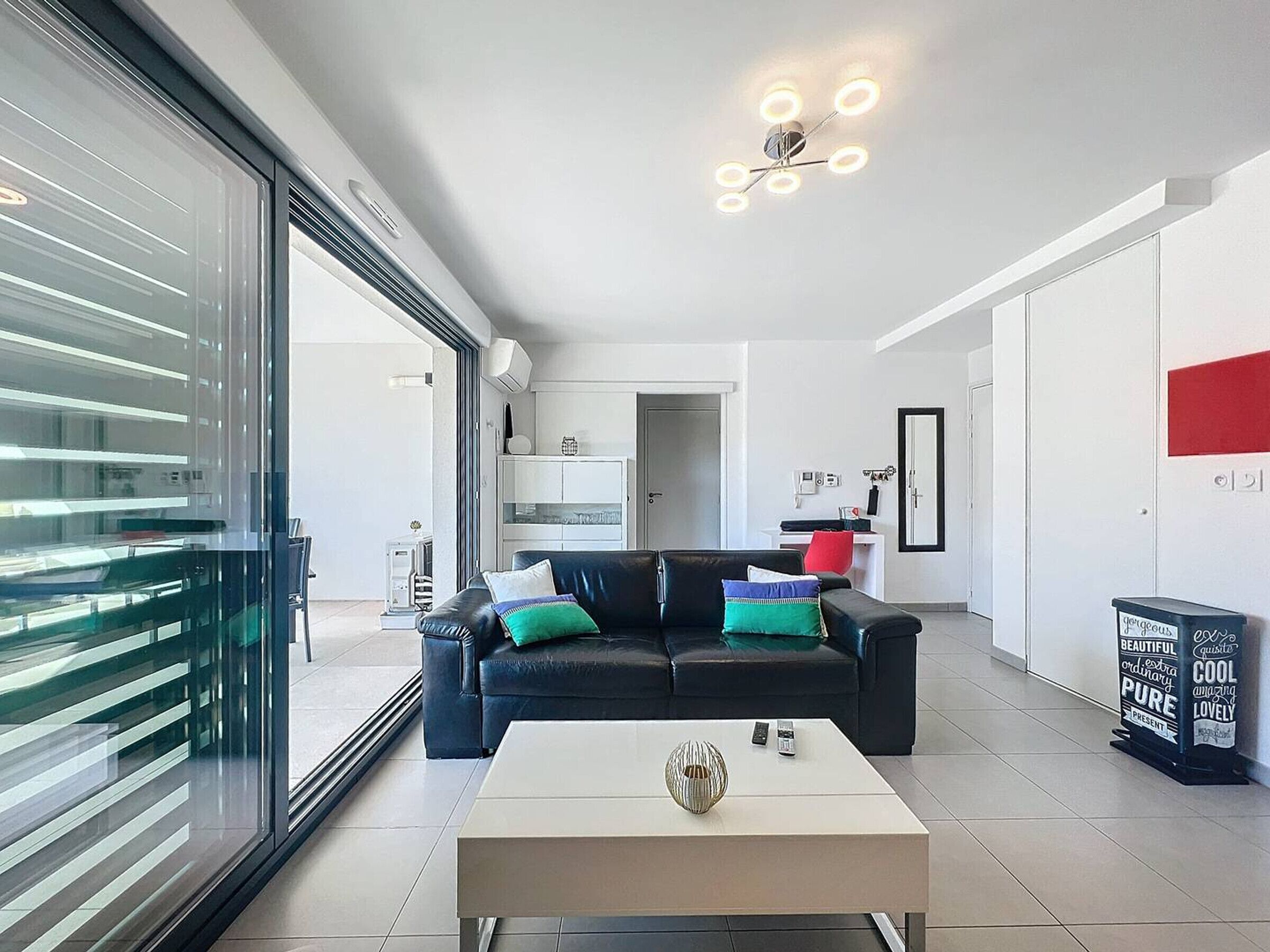 A modern living room with a black leather sofa, a white coffee table, and a glass door leading to a balcony.