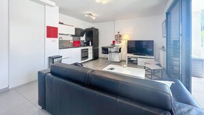 Ett modernt vardagsrum med en svart lädersoffa, en matplats med tv och ett kök med vita skåp och en röd accentvägg.