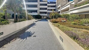 En modern byggnad med flera våningar och en central innergård, omgiven av grönska och palmer.