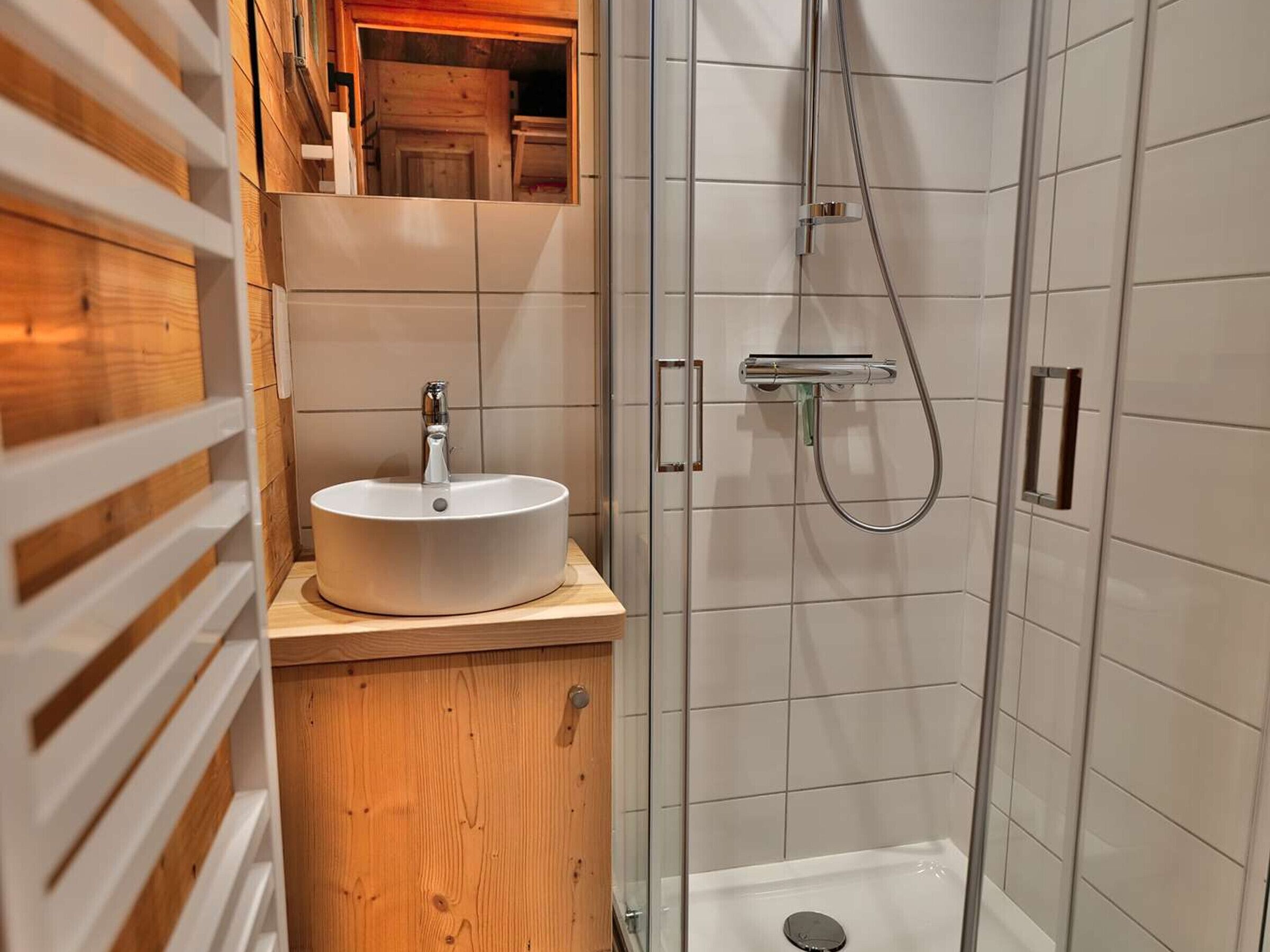 Un baño moderno con un tocador de madera, un lavabo blanco y cabina de ducha con mampara de vidrio.