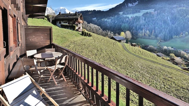 Eine Holzterrasse mit Gartenmöbeln, die auf eine gebirgige Landschaft blickt.