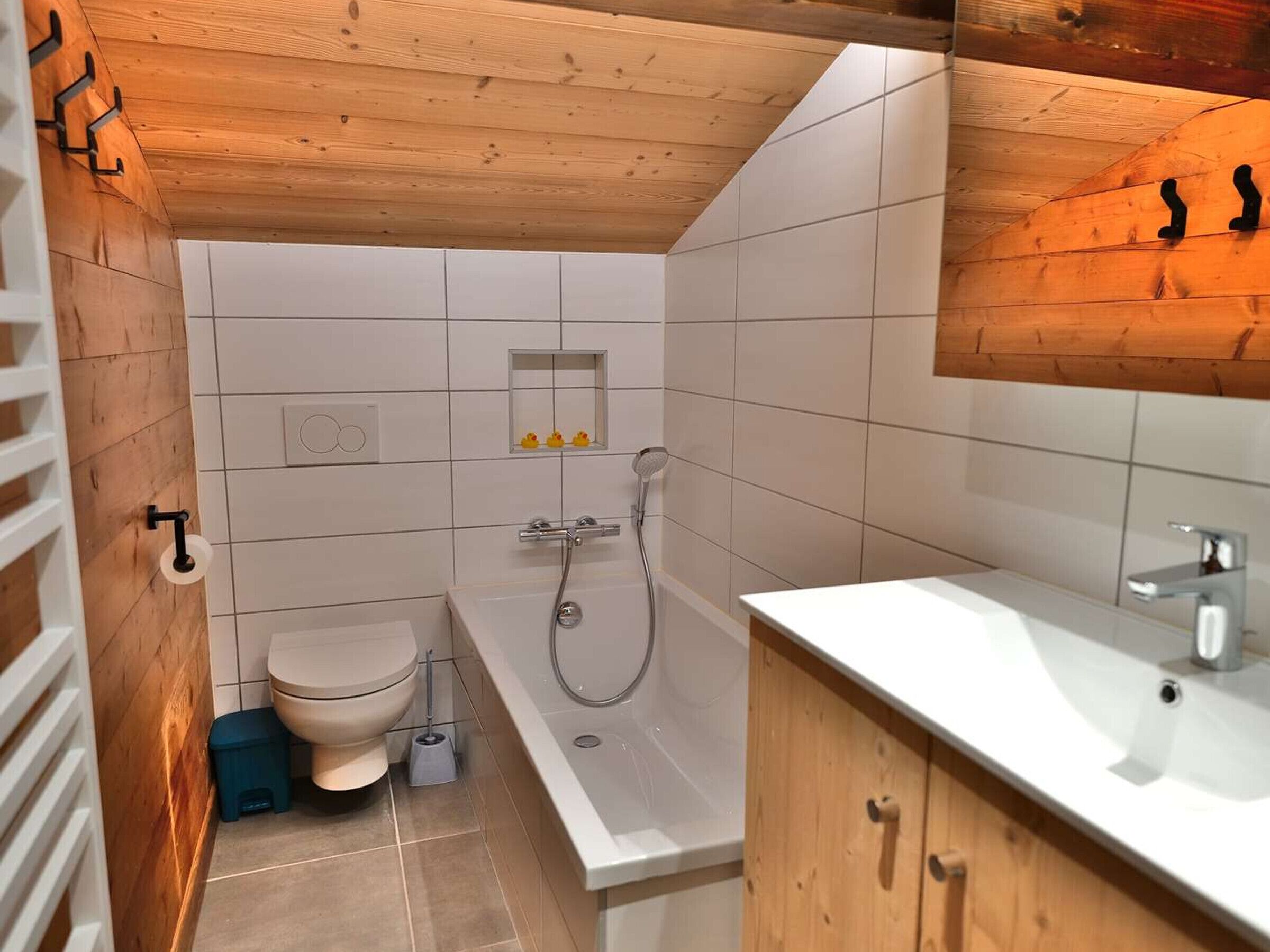Ein kleines Badezimmer mit Toilette, Dusche und Waschbecken, mit Holzboden und weißen Fliesenwänden.