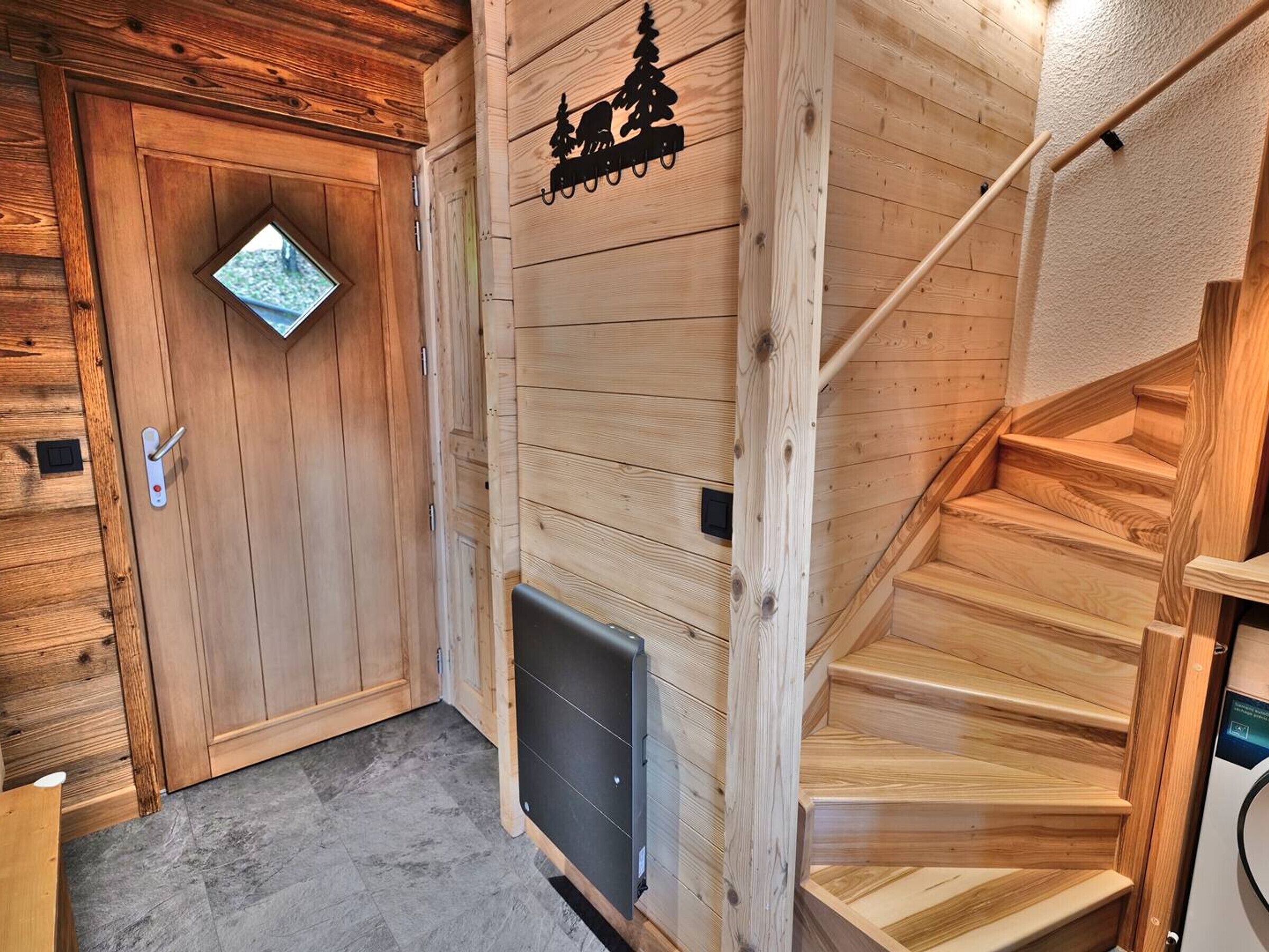 L’intérieur d’un chalet en bois, avec un escalier en bois, une porte dotée d’une fenêtre et un panneau fixé au mur.