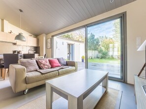 Un salon moderne avec un canapé, une table basse et une grande porte-fenêtre coulissante donnant sur un jardin.