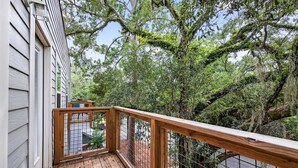 Eine Holzterrasse mit Metallgeländer, umgeben von üppigem Grün und Bäumen.
