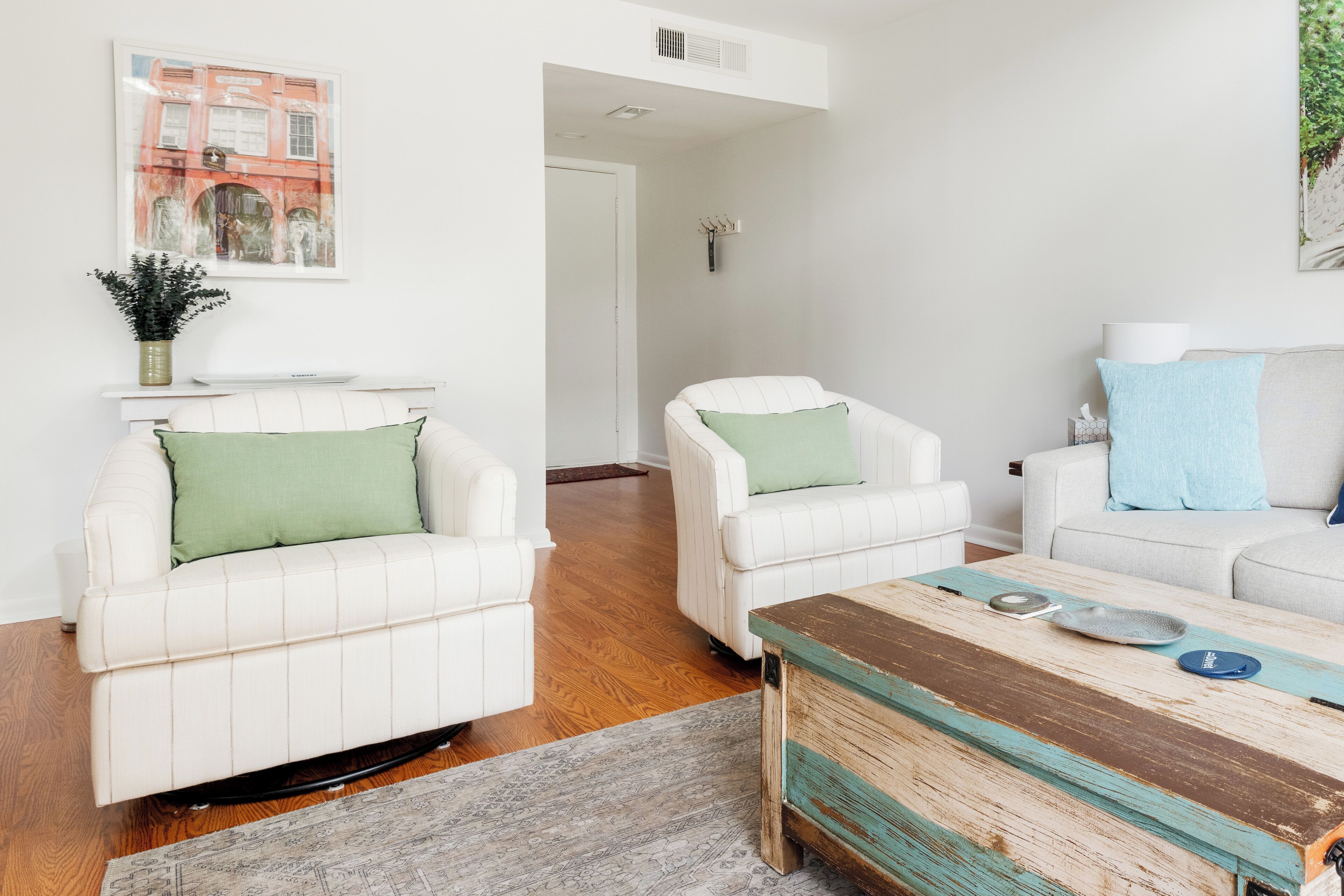 A modern living room with white leather sofas, a wooden coffee table, and a framed cityscape picture on the wall.