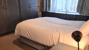 Een net opgemaakt bed in een kamer met donkere houten kasten en een raam met gordijnen.