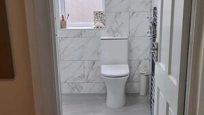 Een badkamer met toilet, marmeren wanden en een raam met decoratie.