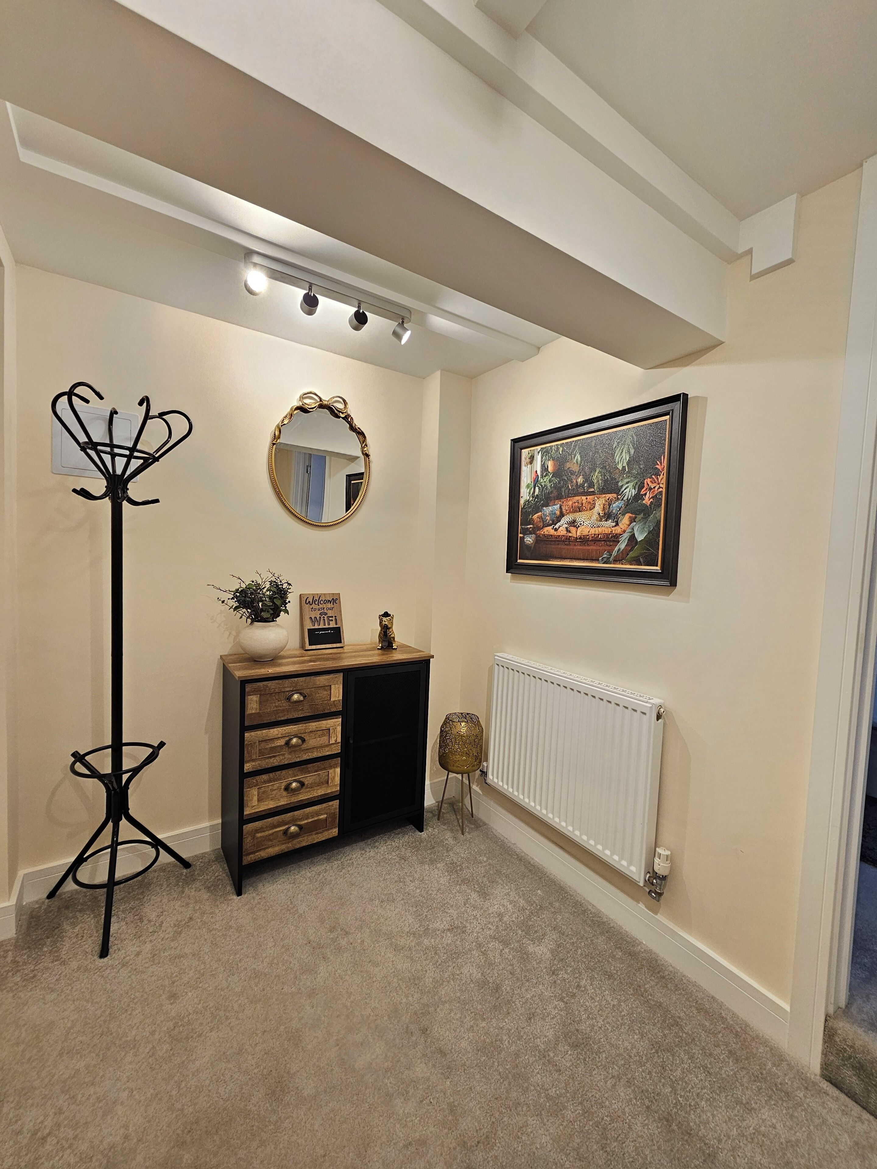 Une pièce comprenant une commode en bois, un miroir, un radiateur et un tableau encadré accroché au mur.