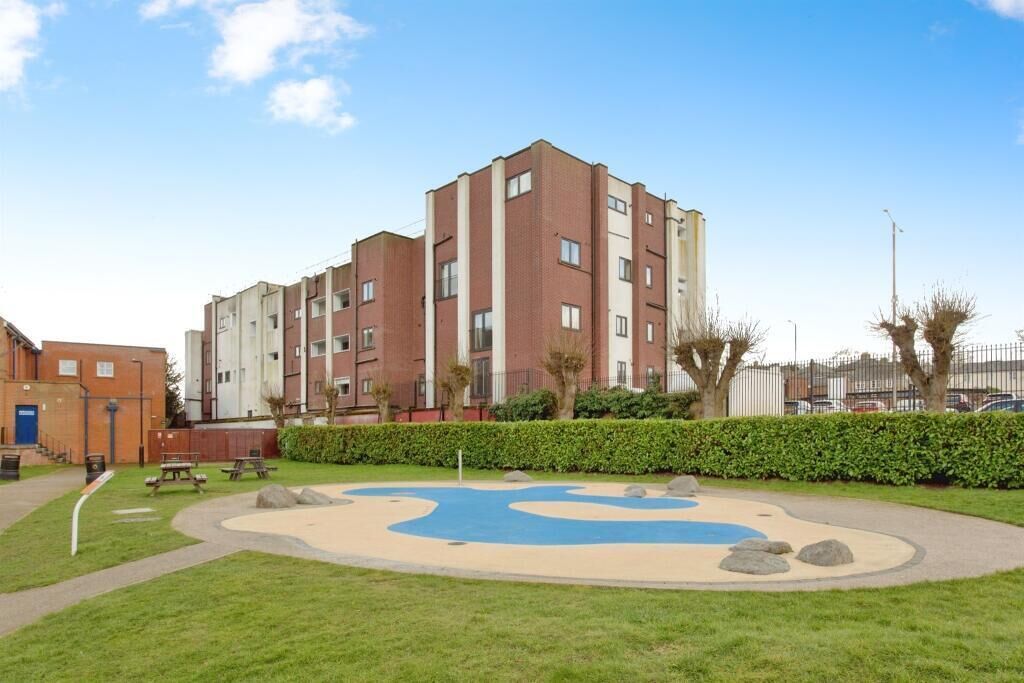 A multi-story residential building with a courtyard featuring a blue play area and picnic tables.
