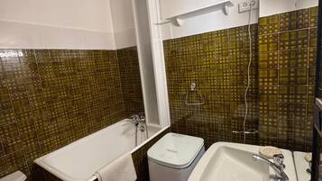 A bathroom with a bathtub, toilet, sink, and a trash bin.