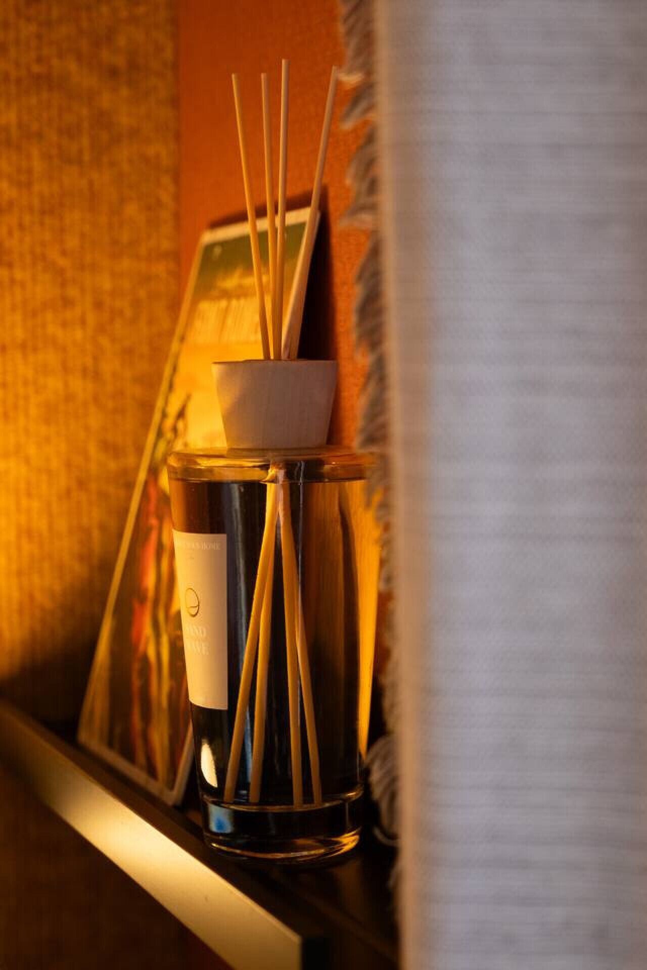 A candle holder with a candle and incense sticks on a shelf.