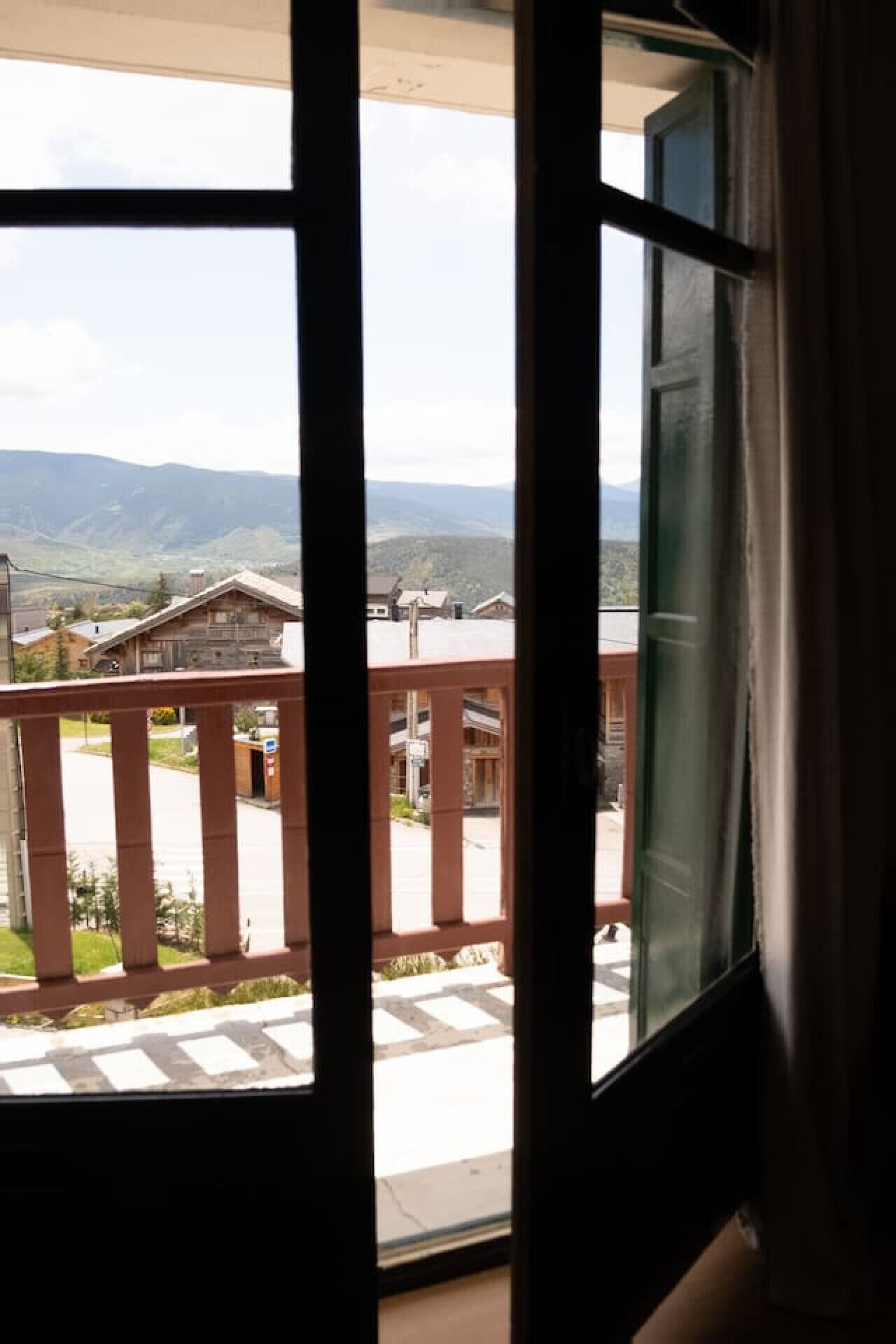 Vista des d'un balcó amb barana de fusta, sobre zones residencials amb cases i muntanyes a la distància.