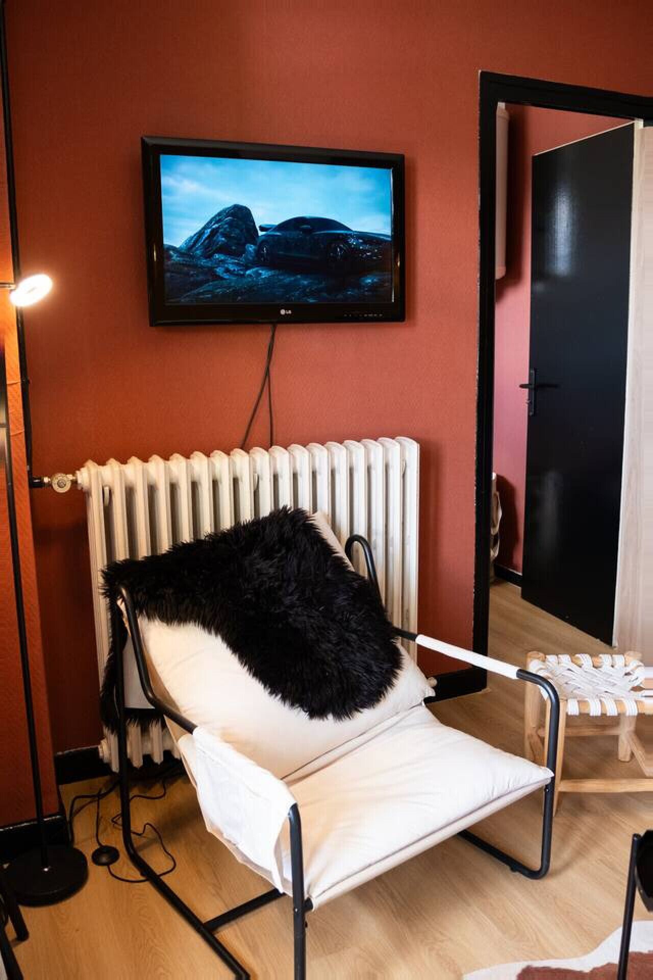 A room with a white radiator, a black furry chair, a television on the wall, and a door.