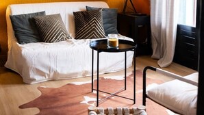 Een gezellige woonkamer met een bank, een klein rond tafeltje met een kaars, een houten stoel en een kussen van leer.