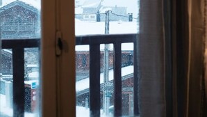 Uitzicht door een raam met een witte lijst, gordijnen zijn deels open, en een besneeuwd landschap buiten.