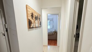 Ein Flur mit Holzboden, weißen Wänden und einer Tür rechts. Auf der linken Wand hängt ein Bild von Palmen.
