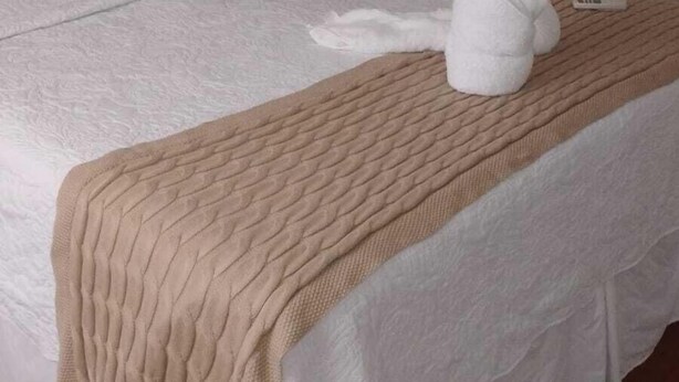 Ein ordentlich bezogenes Bett mit einer beigen Decke, weißen Kissen und zwei weißen Handtüchern.