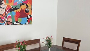 Ein Esstisch mit zwei weißen Vasen voller Blumen, Holzstühlen und einem farbenfrohen, abstrakten Gemälde an der Wand.