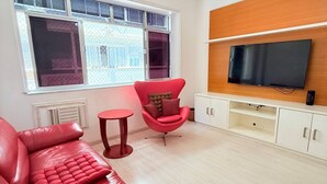 Ein modernes Wohnzimmer mit einem roten Ledersofa, einem roten Sessel, einem Fernseher an einer Holzwand und einem Fenster mit Jalousien.