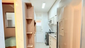 Eine schmale Küche mit einer eingebauten Holzregaleinheit, einem Edelstahlkühlschrank und einer Mikrowelle.