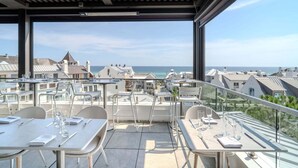 En tagterrasse med borde og stole, med udsigt over en kystnær by.