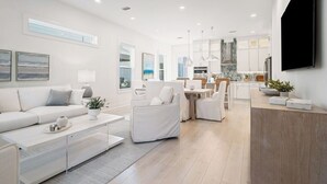 A modern living room with a sofa, coffee table, and a dining area with chairs and a table. - Luxury Home, Sleeps 16, Palm & Pearl, Pool, Inlet Beach (Inlet Beach)