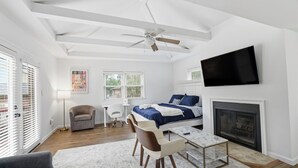 Ein modernes Schlafzimmer mit Bett, Fernseher, Kamin und Deckenventilator.
