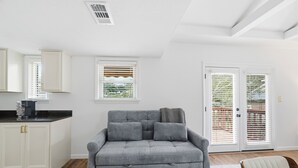 Ein modernes Wohnzimmer mit grauem Sofa, weißen Schränken und einer Küchenzeile.