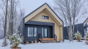A modern house with a dark exterior, a wooden front porch, and a sloped roof. - Kos - Domaine du Grand Portneuf - Spa, Nature & Co (Pont-Rouge)