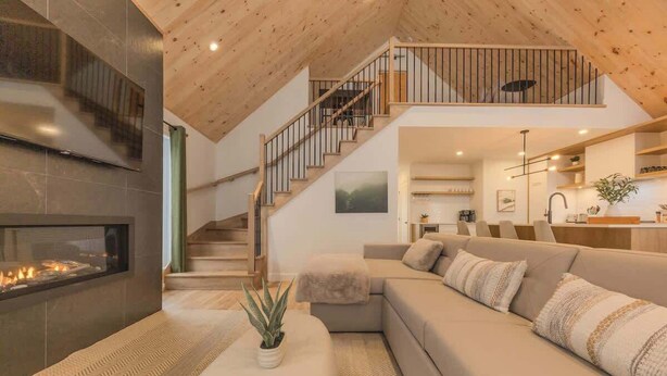 A modern living room with a fireplace, a sofa, a staircase, and a kitchen area. - Kos - Domaine du Grand Portneuf - Spa, Nature & Co (Pont-Rouge)