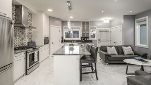 A modern kitchen with a central island, built-in appliances, and a dining area with a sofa and coffee table. - 👑Luxury Inner City New Built /Garage /AC/EV Charger (Calgary)
