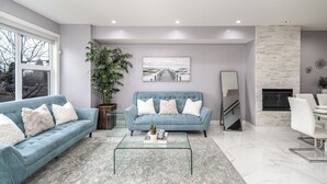 A modern living room with two blue sofas, a glass coffee table, a large potted plant, and a fireplace. - 👑Luxury Inner City New Built /Garage /AC/EV Charger (Calgary)