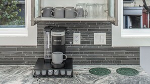 A kitchen with a built-in window shelf holding wine glasses and mugs, a Keurig coffee maker, and a backsplash with a brick pattern. - 👑Luxury Inner City New Built /Garage /AC/EV Charger (Calgary)