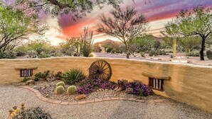 A desert landscape with a rustic stone wall, a wooden wagon wheel, and cacti. - Private, Peaceful, and Spacious Desert Tucson Villa with Heated Pool and Hot Tub (Tucson)