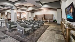 Une pièce spacieuse au design moderne, avec une rangée de fauteuils gris, un grand téléviseur à écran plat fixé au mur et un sol recouvert de carreaux de pierre.