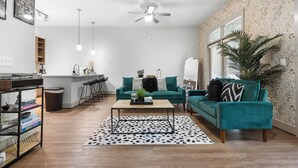 Un salon moderne avec un canapé de couleur turquoise, une table basse et une cuisine en arrière-plan.