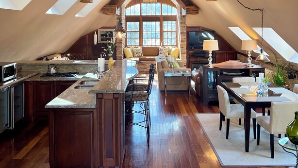 An attic-style kitchen with a central island, wooden beams, skylights, and a view to the living area. - Executive Waterfront Loft- 30+ Days (Mississauga)