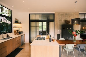 A modern kitchen with a central island, built-in appliances, and a dining area with chairs. - Raw. Tropical. Unique. Villa Madom by NP Marino Ballena (Osa)