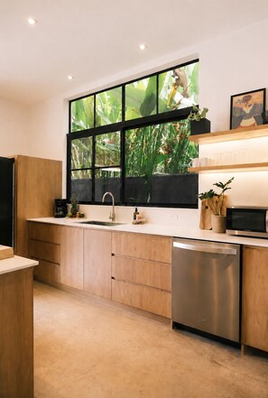 A modern kitchen with a large window, stainless steel appliances, wooden cabinets, and a countertop with various items. - Raw. Tropical. Unique. Villa Madom by NP Marino Ballena (Osa)