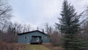 A small, single-story building with a gabled roof, a front porch, and a door. - Cottage On The Lake (Pine Dock)